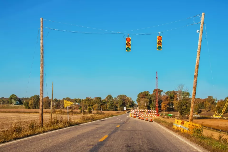 Two-lane rural road with stoplights hanging above roadway and construction visible in distance.